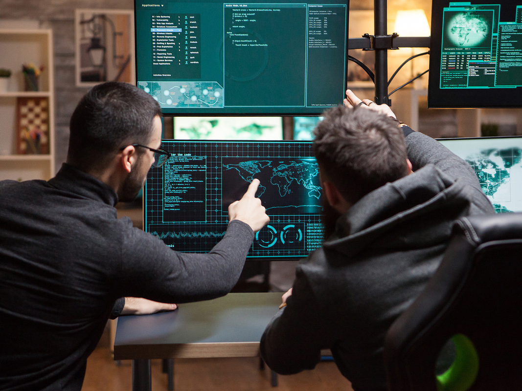 Two people looking at a computer screen and coding while sitting at a desk.
