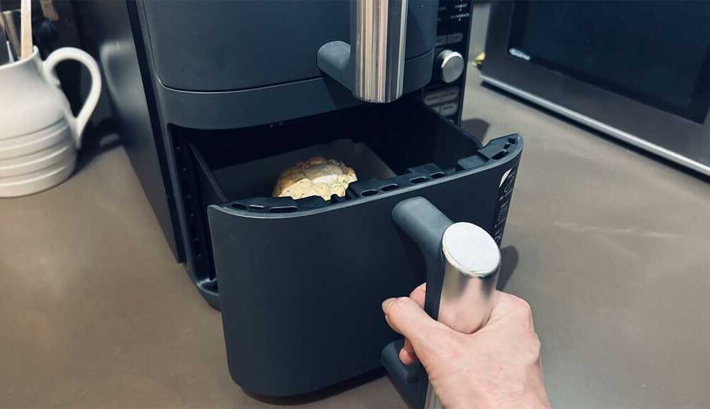 A hand opening an air fryer drawer, with a liner inside