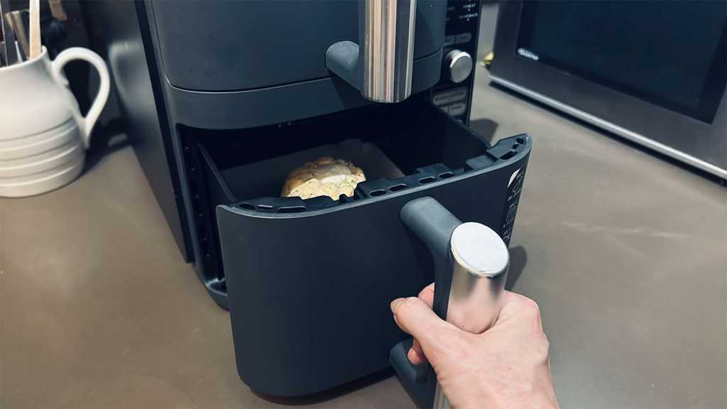 A hand opening an air fryer drawer, with a liner inside