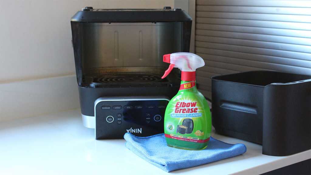 An air fryer turned upside down, with cleaning spray and a cloth in front of it