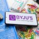 Byju's logo displayed on a smartphone laying on a table covered in school supplies