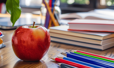 An apple and pens on a school desk.