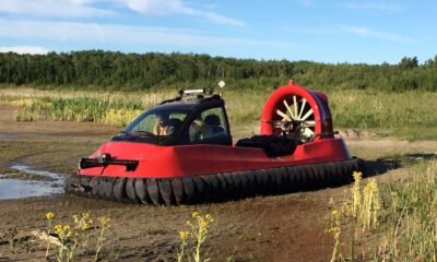 a red hovercraft vehicle sits on the mud with two occupants in the cabin